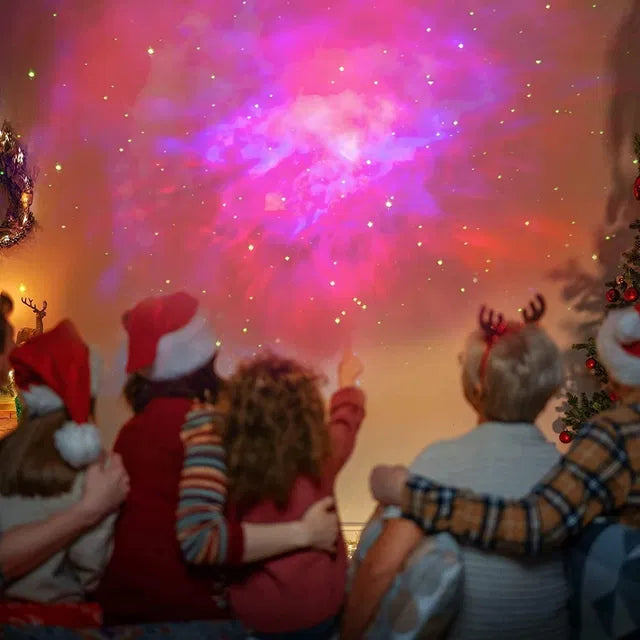 Four kids in festive hats sit together, gazing at galaxy lights from the 22927 Astronaut Galaxy Projector with 360° magnetic head rotation and remote control. One points in awe as a Christmas tree and wreath set a cozy holiday mood.