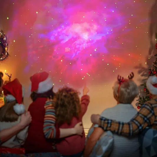 Four kids in festive hats sit together, gazing at galaxy lights from the 22927 Astronaut Galaxy Projector with 360° magnetic head rotation and remote control. One points in awe as a Christmas tree and wreath set a cozy holiday mood.